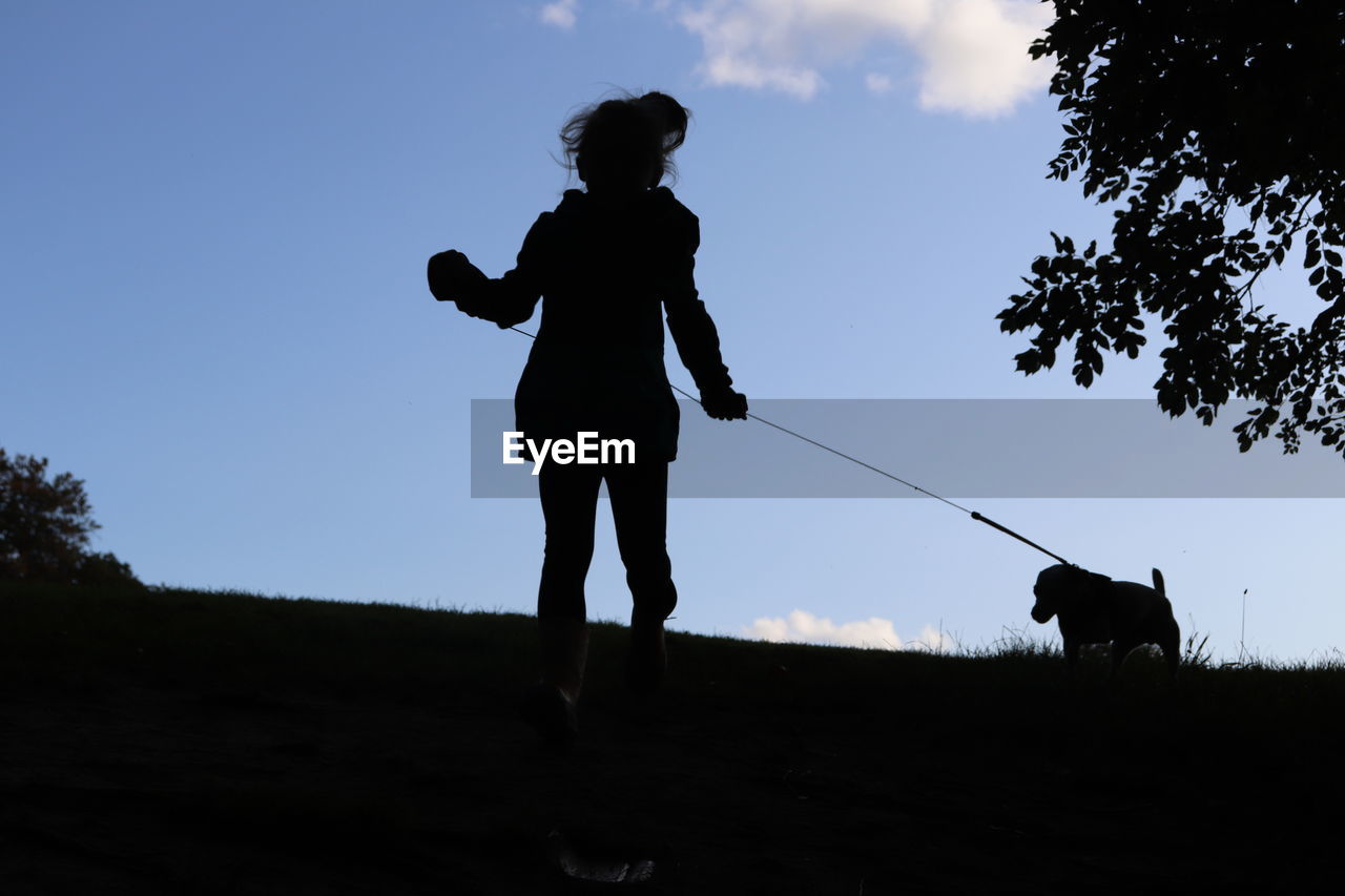 Silhouette girl with dog walking on field