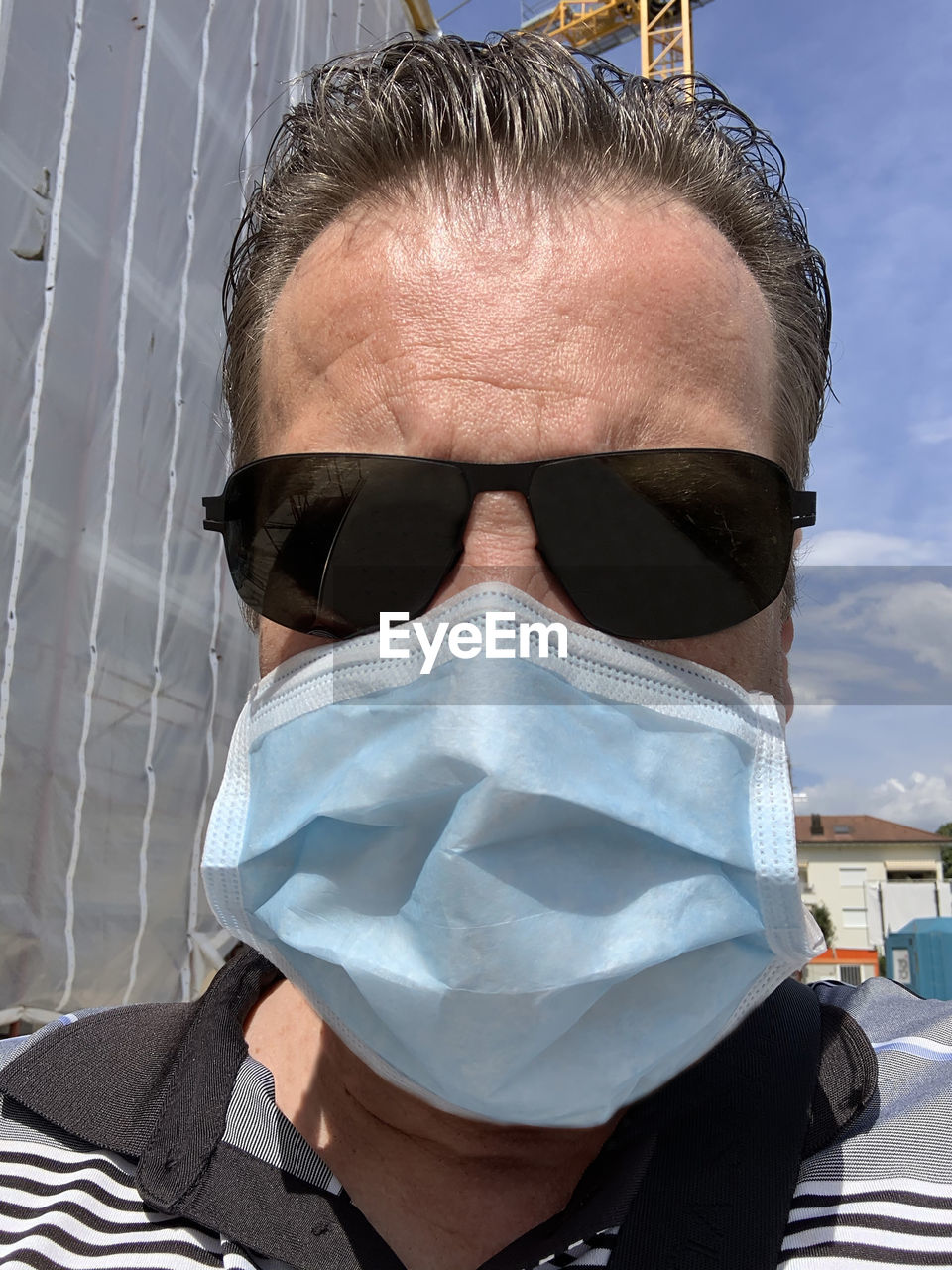 Headshot on a man with face protective mask and sunglasses on a construction site.