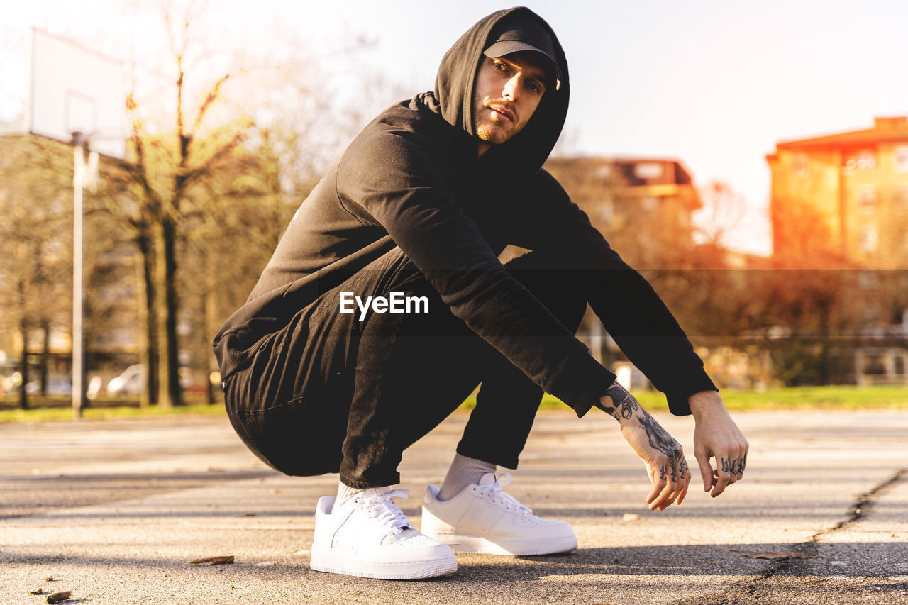 Portrait of young man crouching on land in city