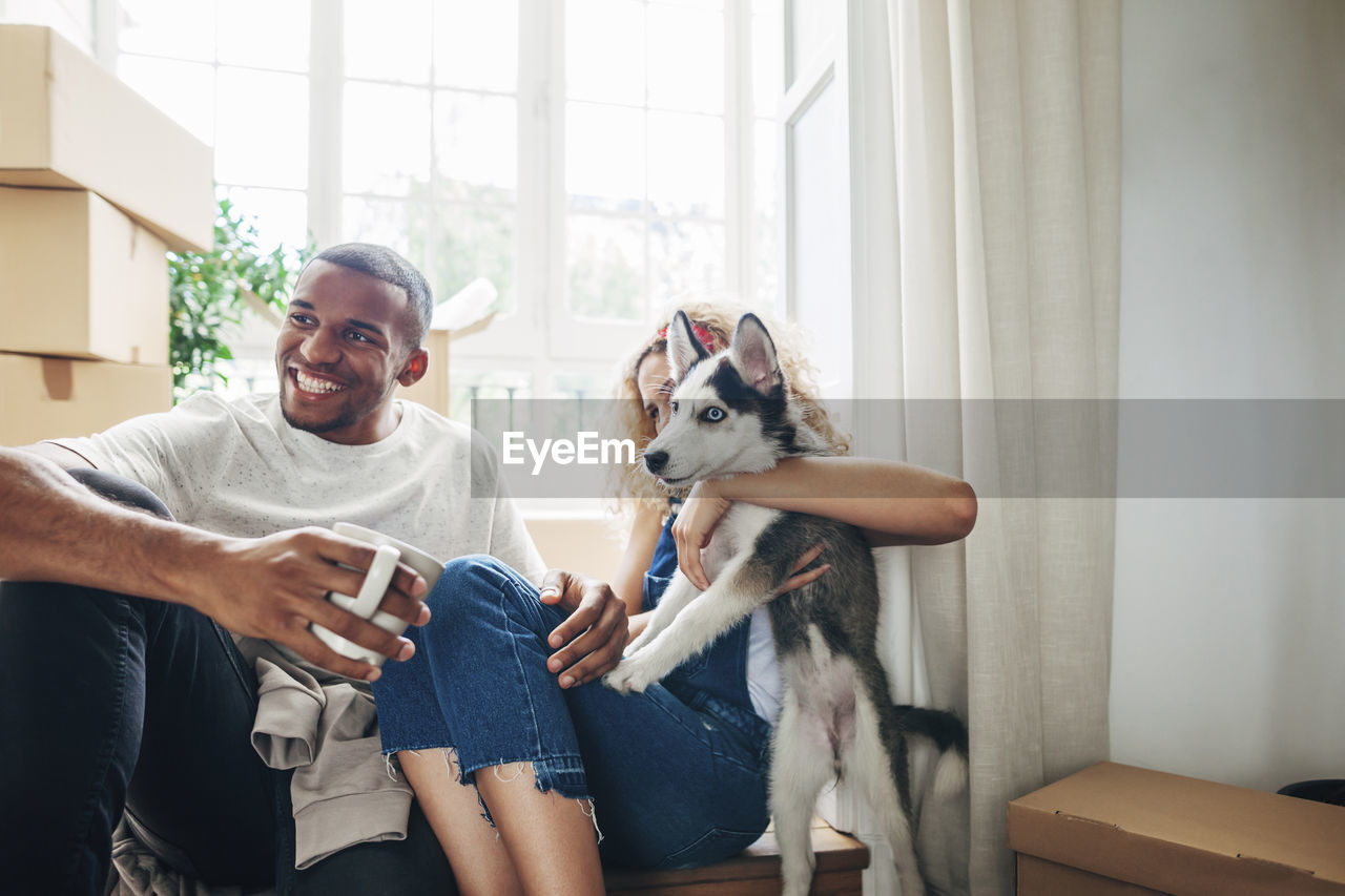 Happy couple with dog sitting at doorway in new house