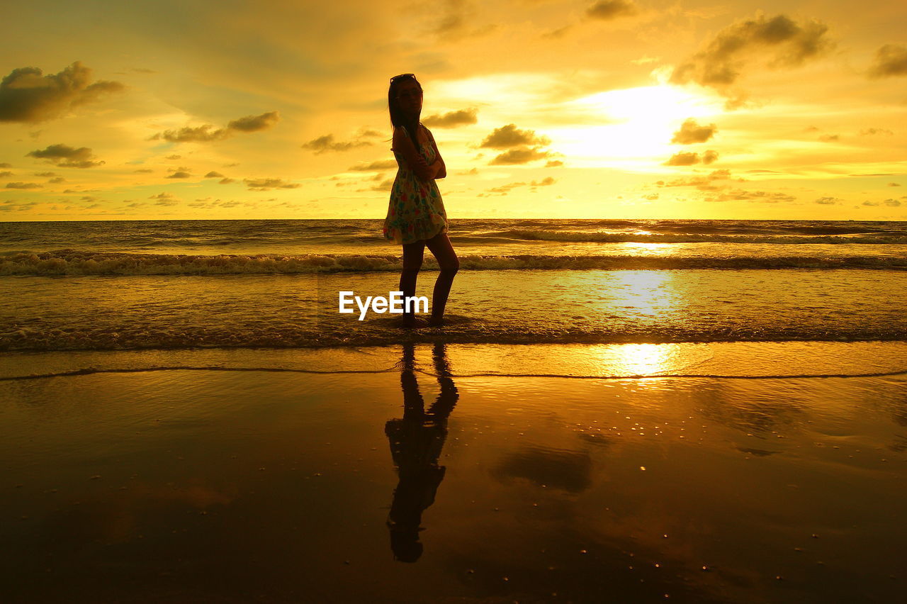 SILHOUETTE WOMAN STANDING ON BEACH AGAINST SKY DURING SUNSET