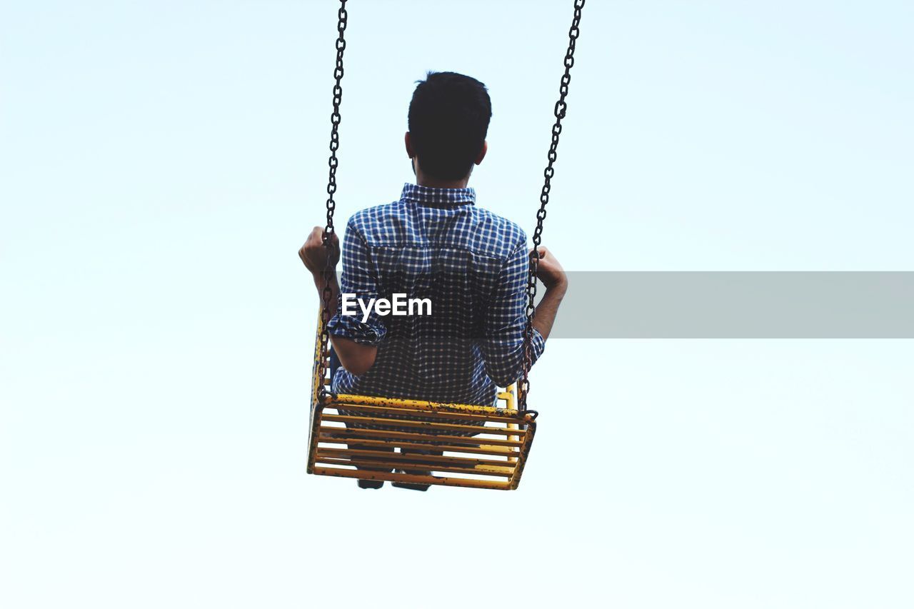 Rear view of man swinging against clear sky