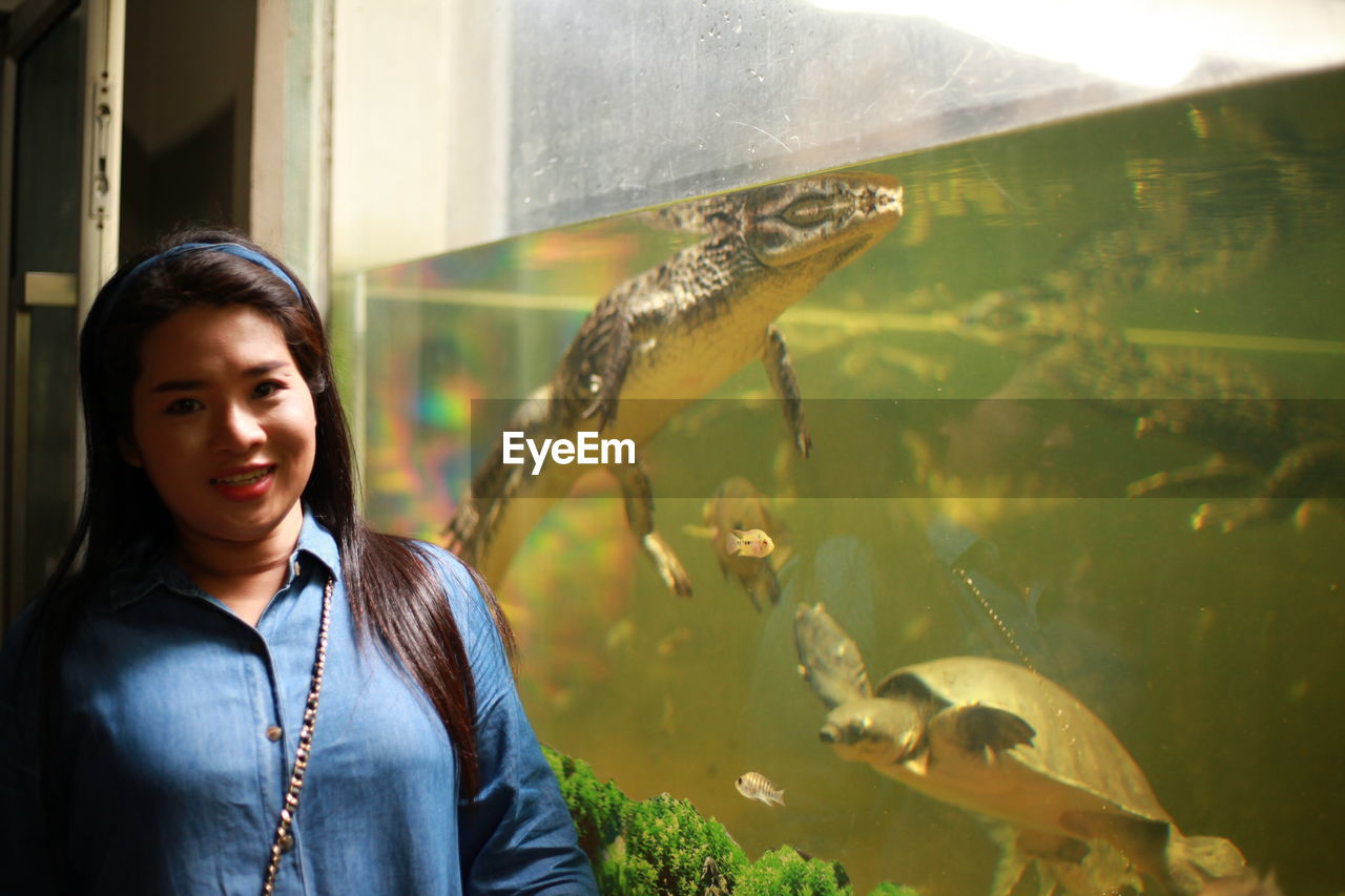 Portrait of woman standing by crocodile in fish tank