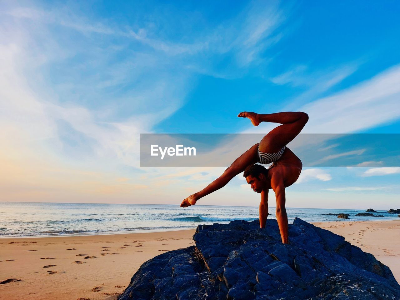 Full length of man exercising at beach against sky during sunset