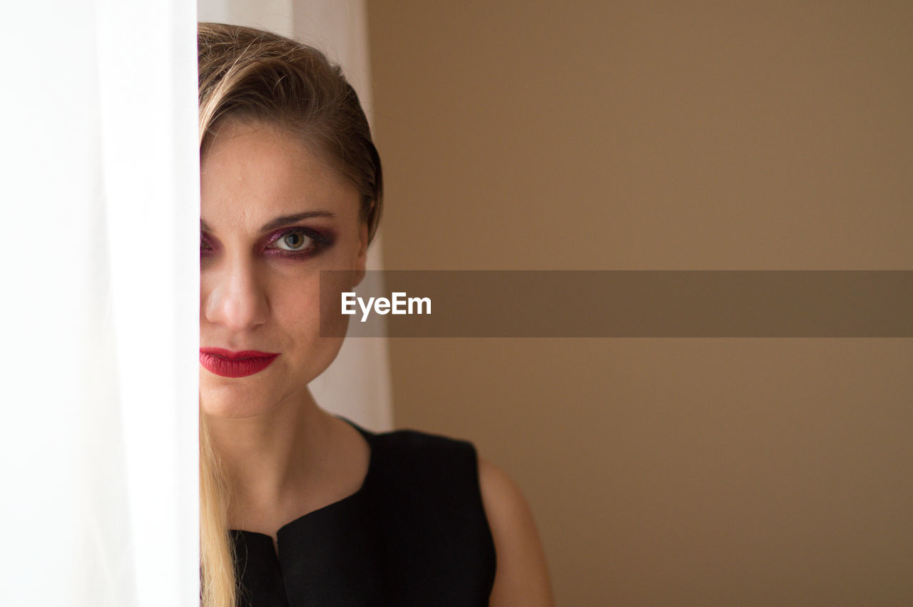 Close-up portrait of woman with spooky eye make-up against wall at home