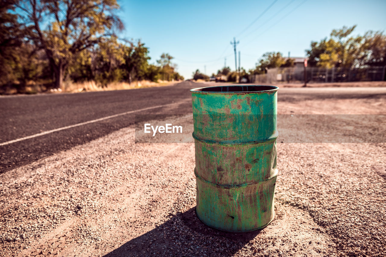 Abandoned green drum by road on sunny day