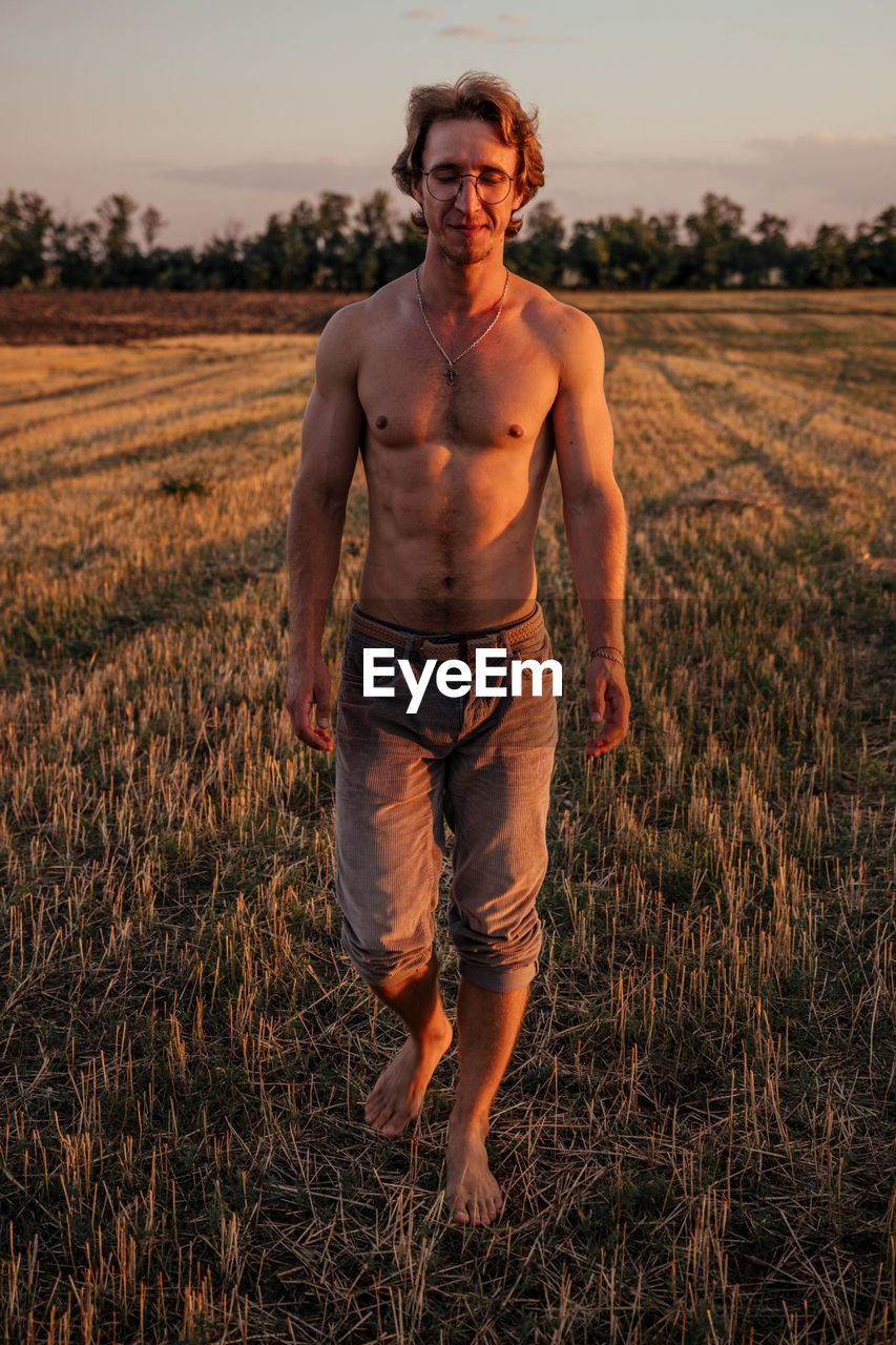 Portrait of shirtless man standing on field