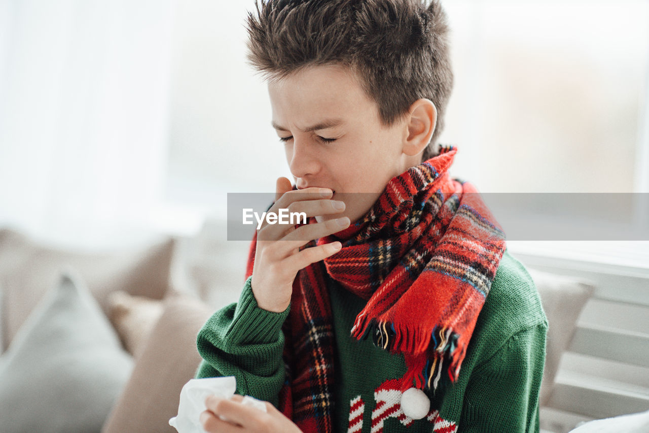 Close-up of boy sneezing at home