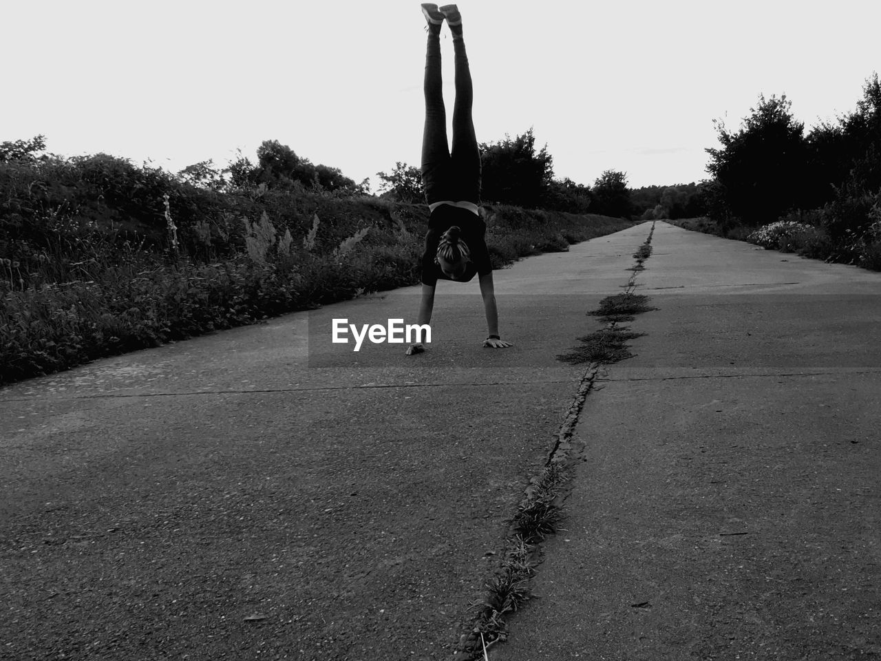Young woman doing handstand on footpath against clear sky