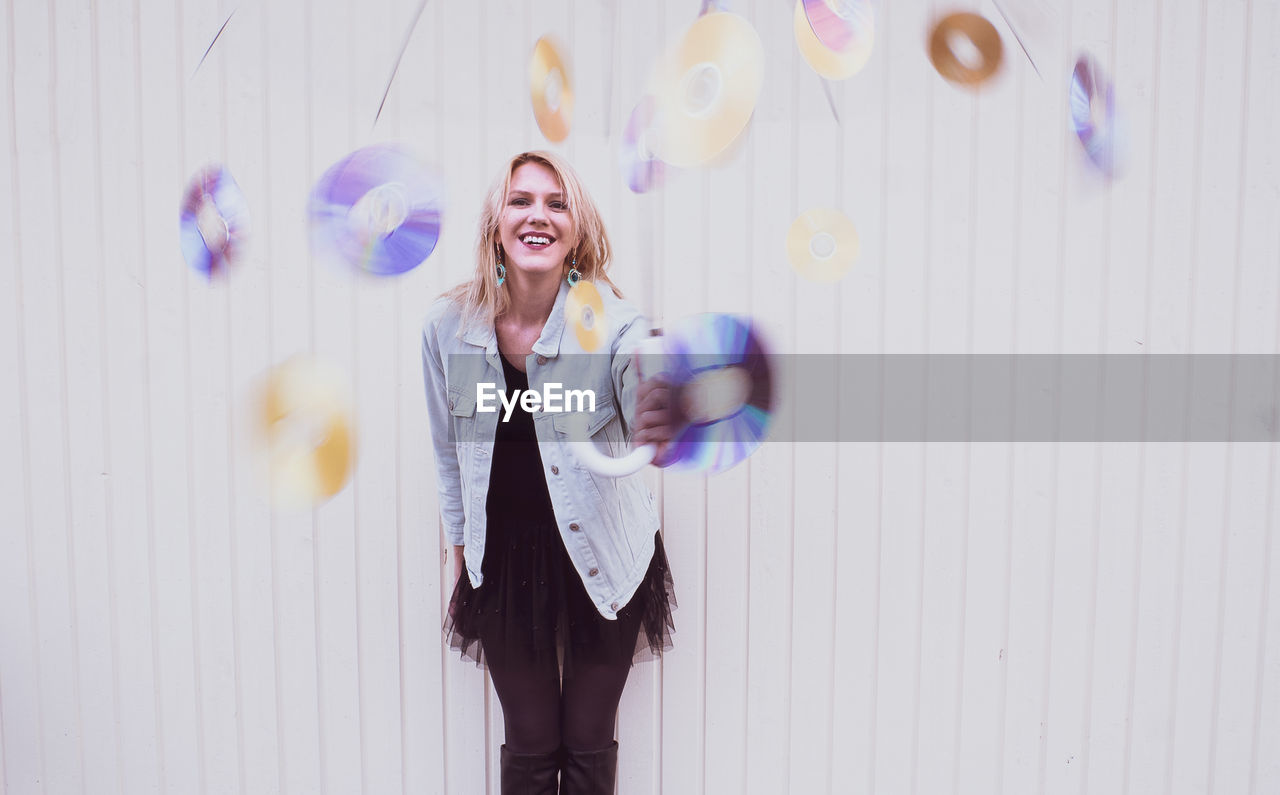 Portrait of a smiling young woman standing against wall