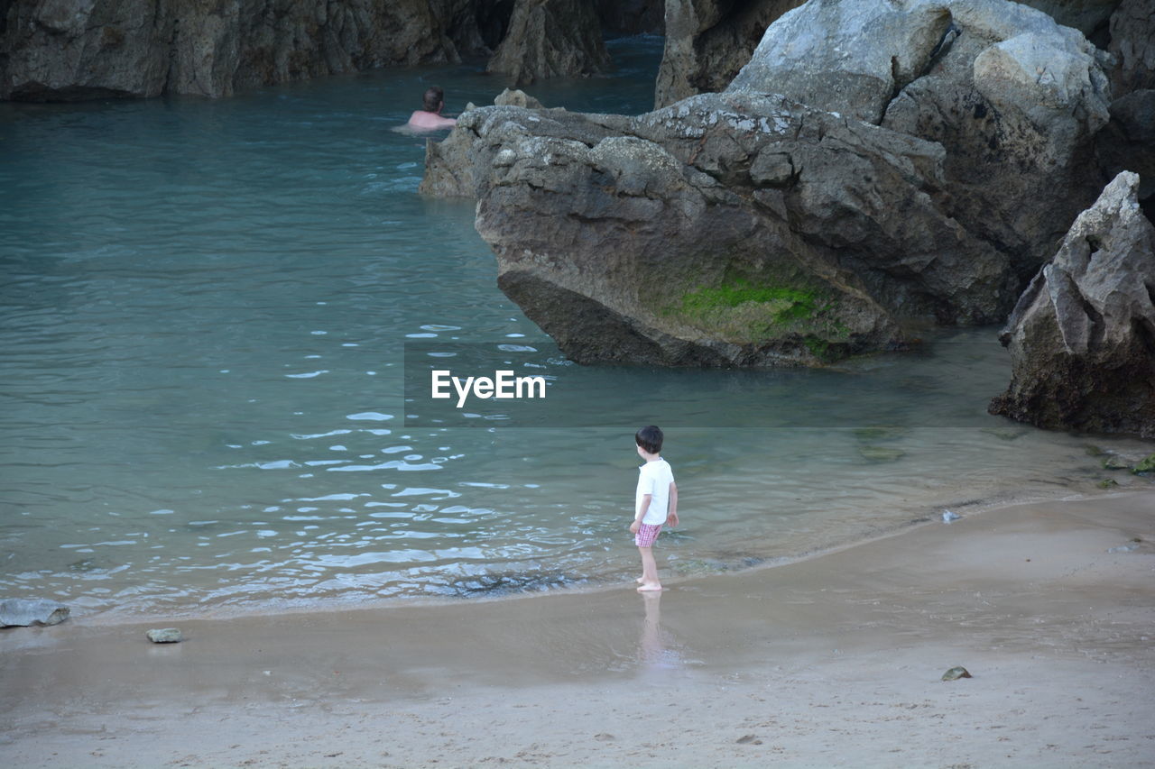 High angle view of boy standing on shore by rock formations