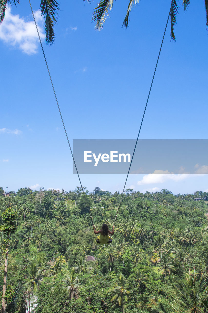 Woman swinging on swing over trees against sky