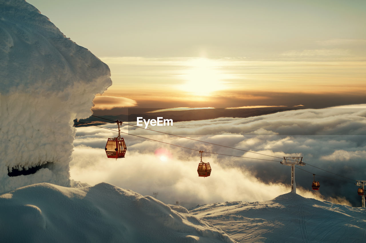 Ski lifts above clouds at sunset
