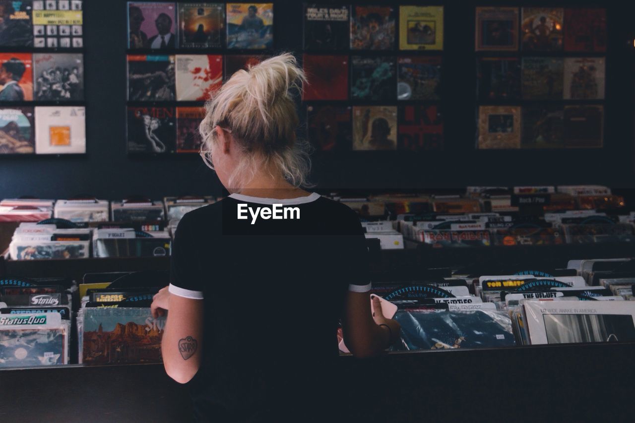 REAR VIEW OF A WOMAN STANDING IN STORE