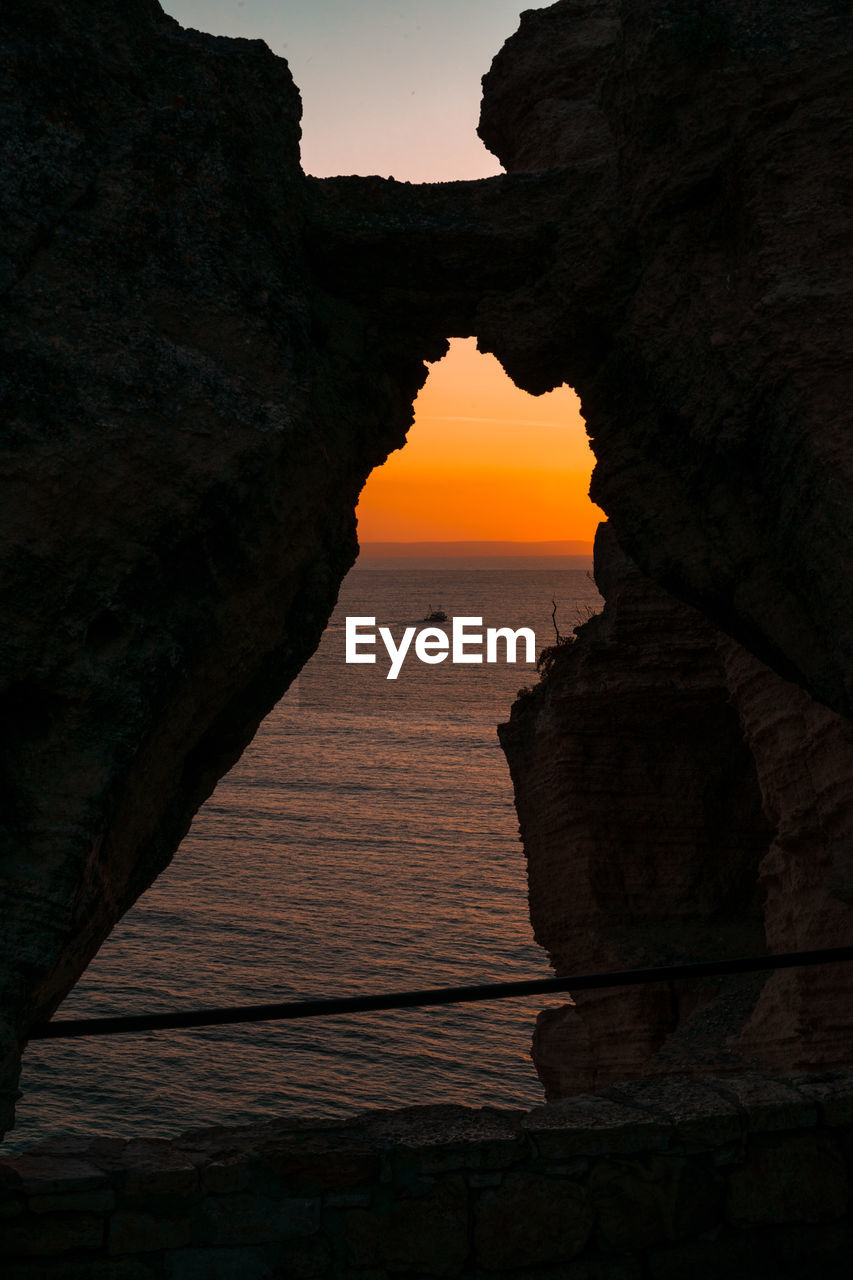 Silhouette rock formation in sea against sky during sunset