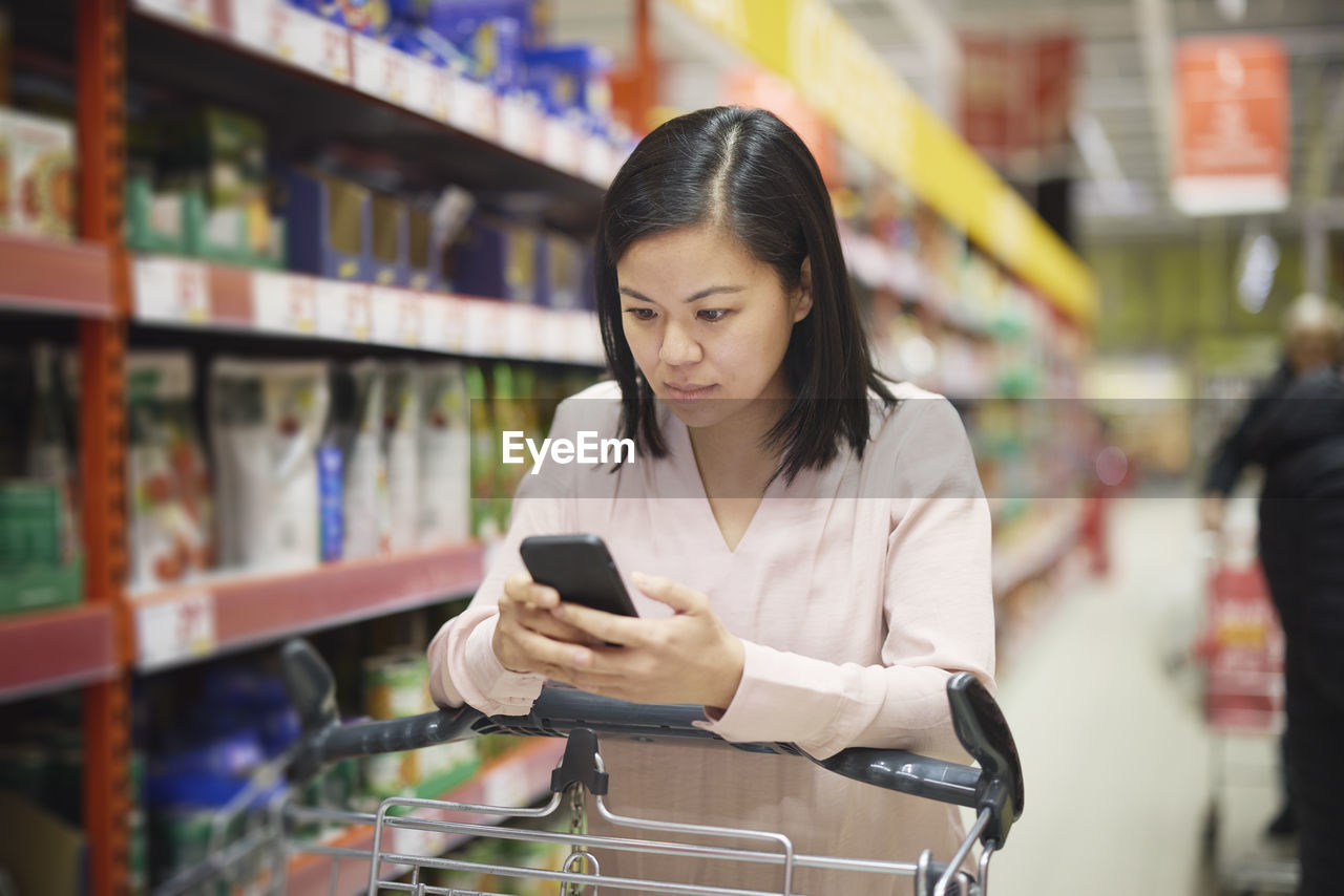 Woman looking at prices during inflation while doing shopping in supermarket