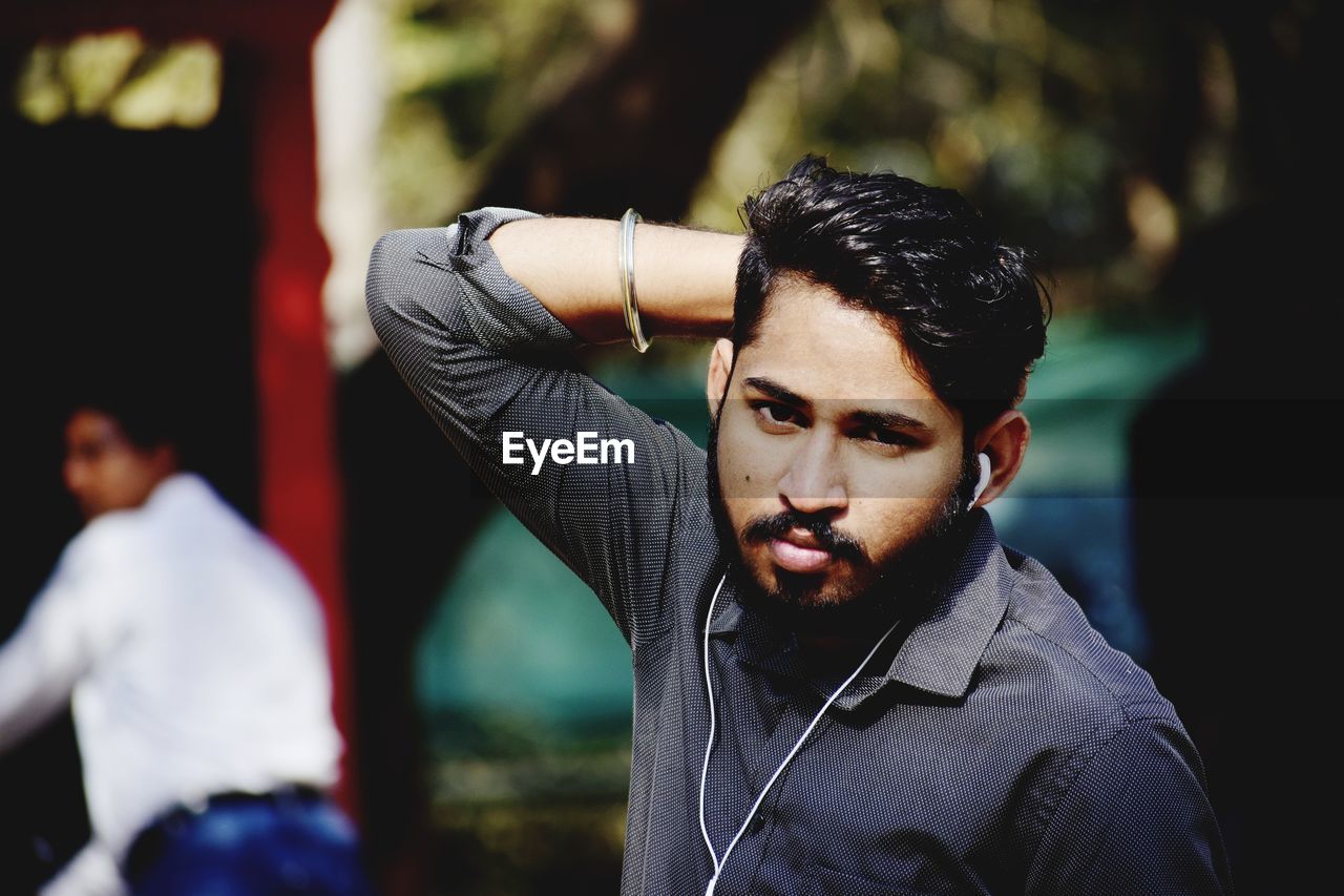 Portrait of young man listening music while standing outdoors