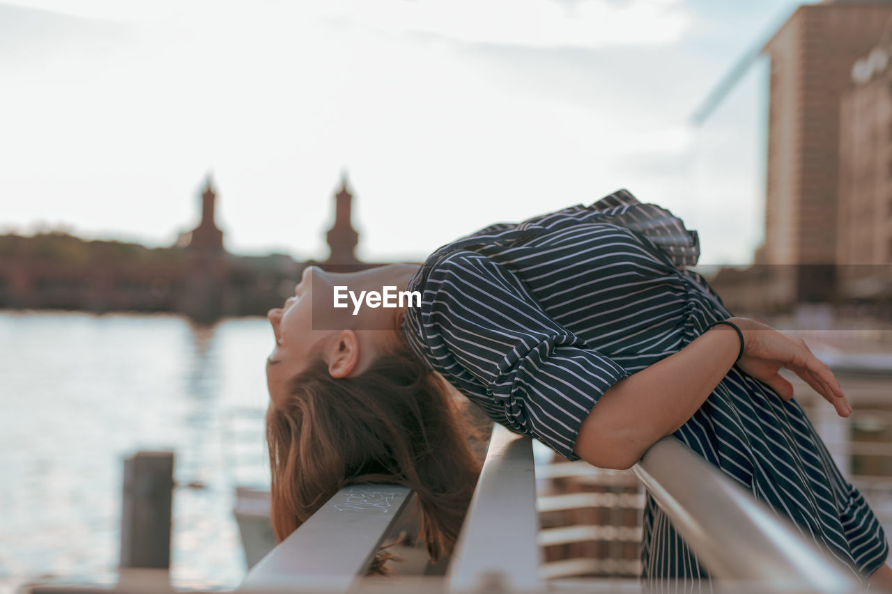 Side view of woman leaning on railing against sky