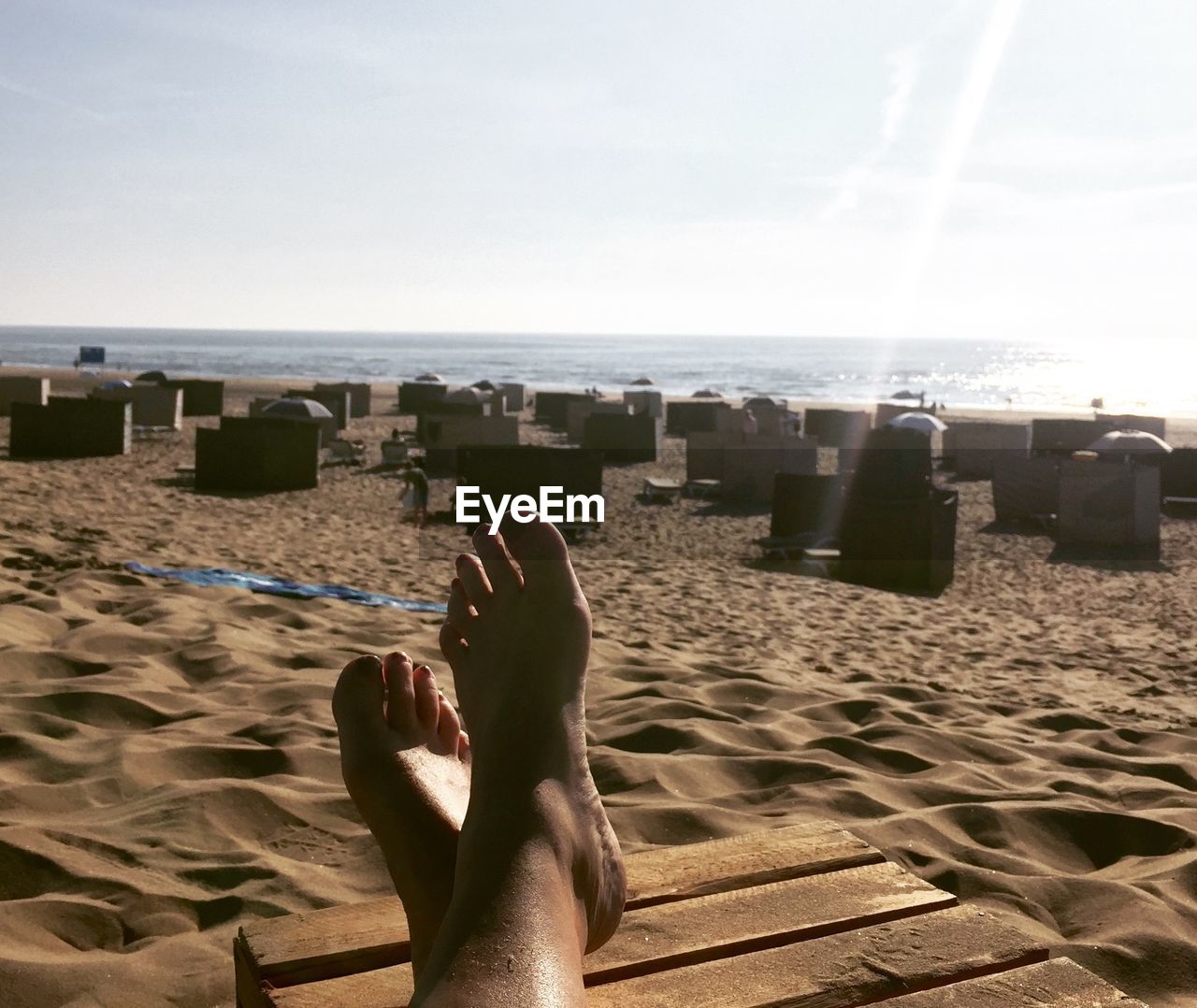 Low section of woman resting on deck chair at beach against sky