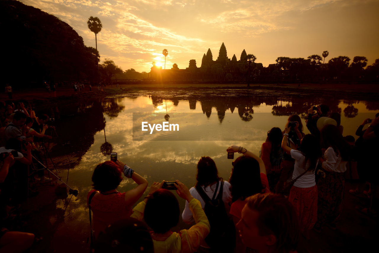 People photographing against lake and sky during sunset