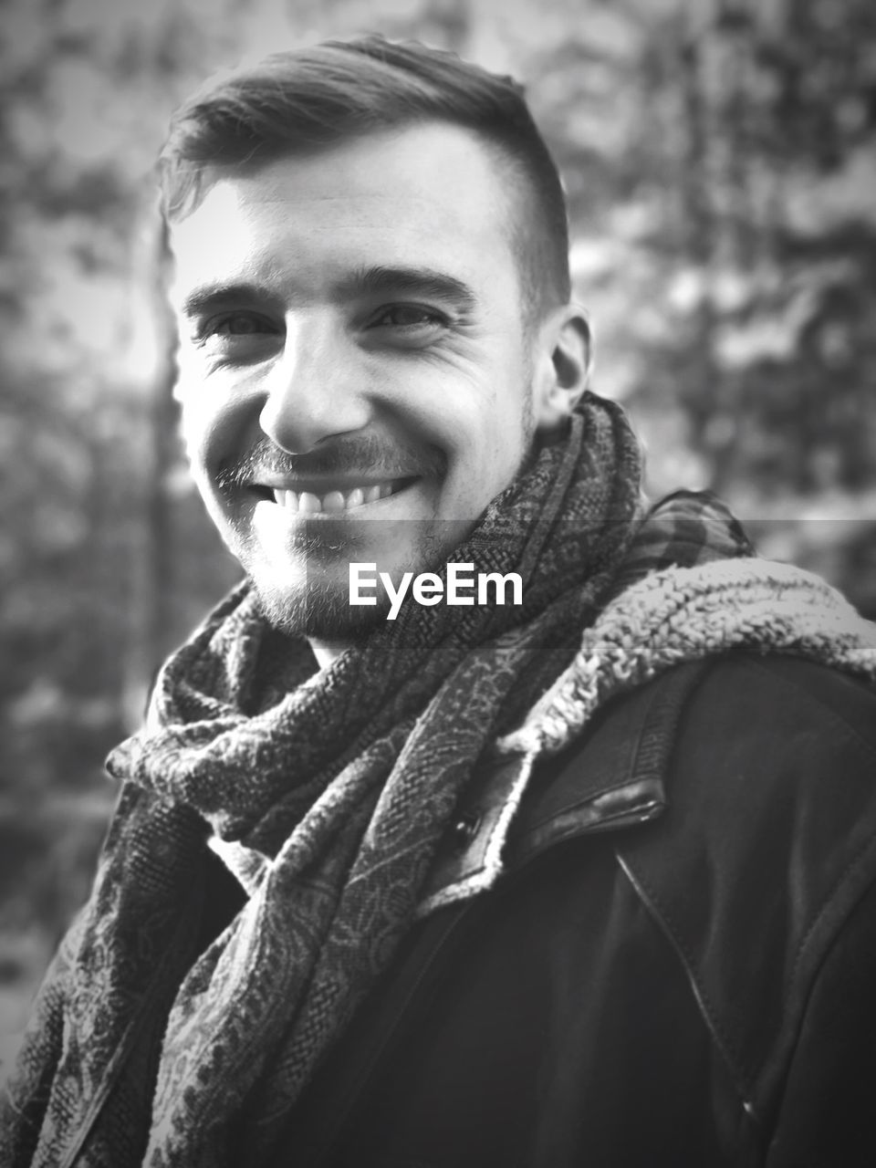 Portrait of smiling young man wearing scarf in forest