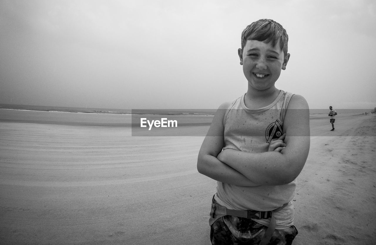 Portrait of smiling boy with arms crossed standing on sand at daytona beach