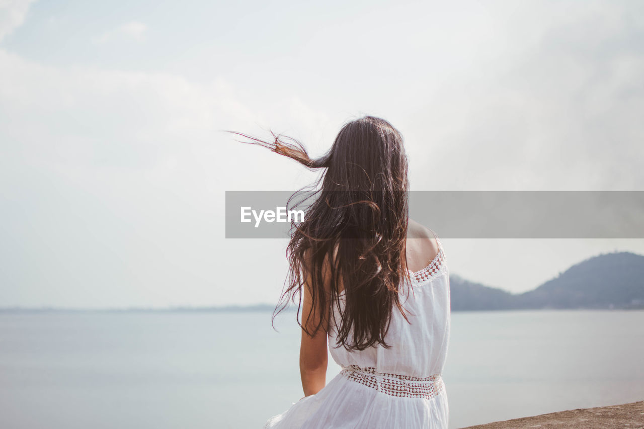 Rear view of woman sitting on retaining wall against sky