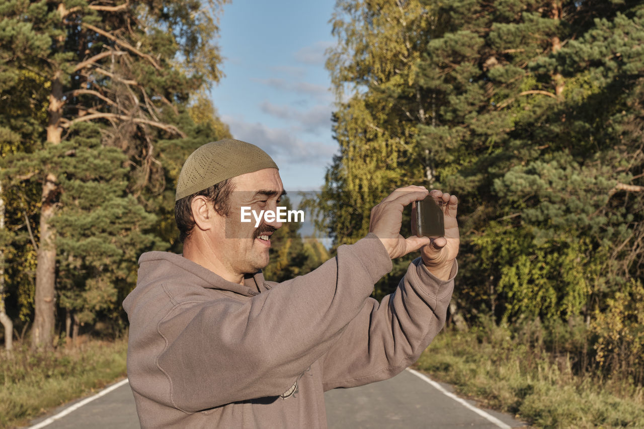 Portrait of man photographing with mobile phone in park

