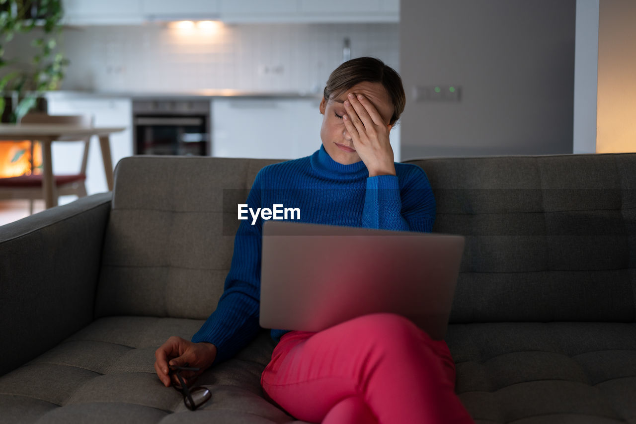 Young woman having headache looks with tired expression after working on business project at home