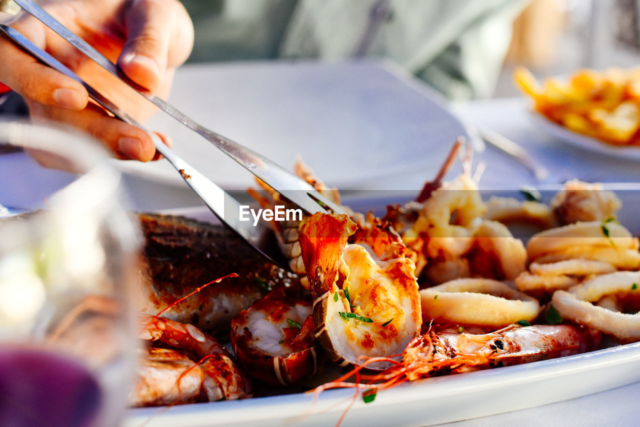 Cropped hand of person holding seafood with serving tong