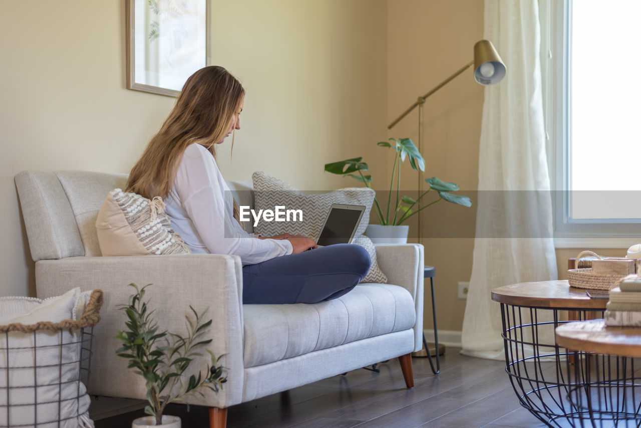 Casual young woman working on laptop at home in stylish living room