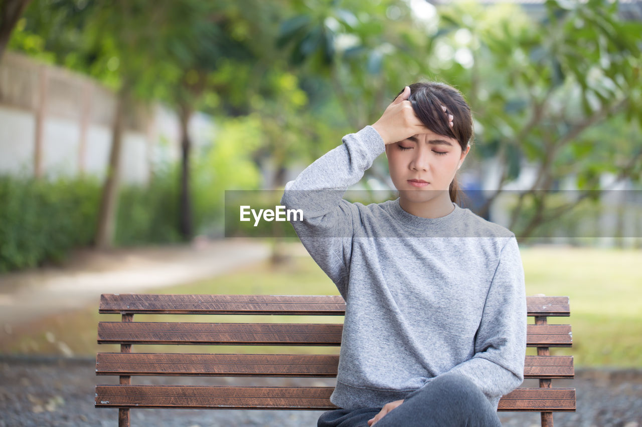 Young woman with headache sitting on park bench