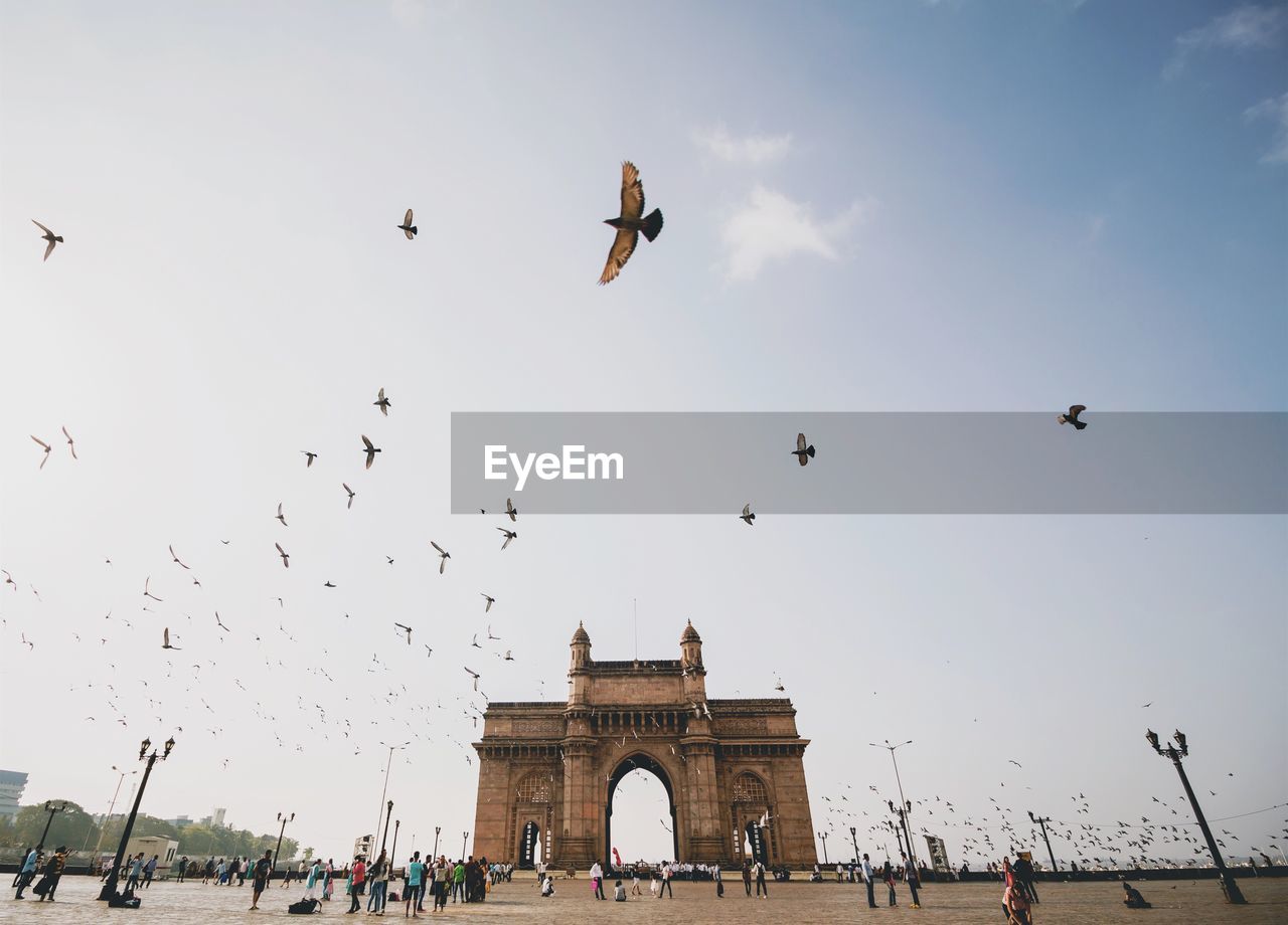 People at gateway to india with birds flying in sky