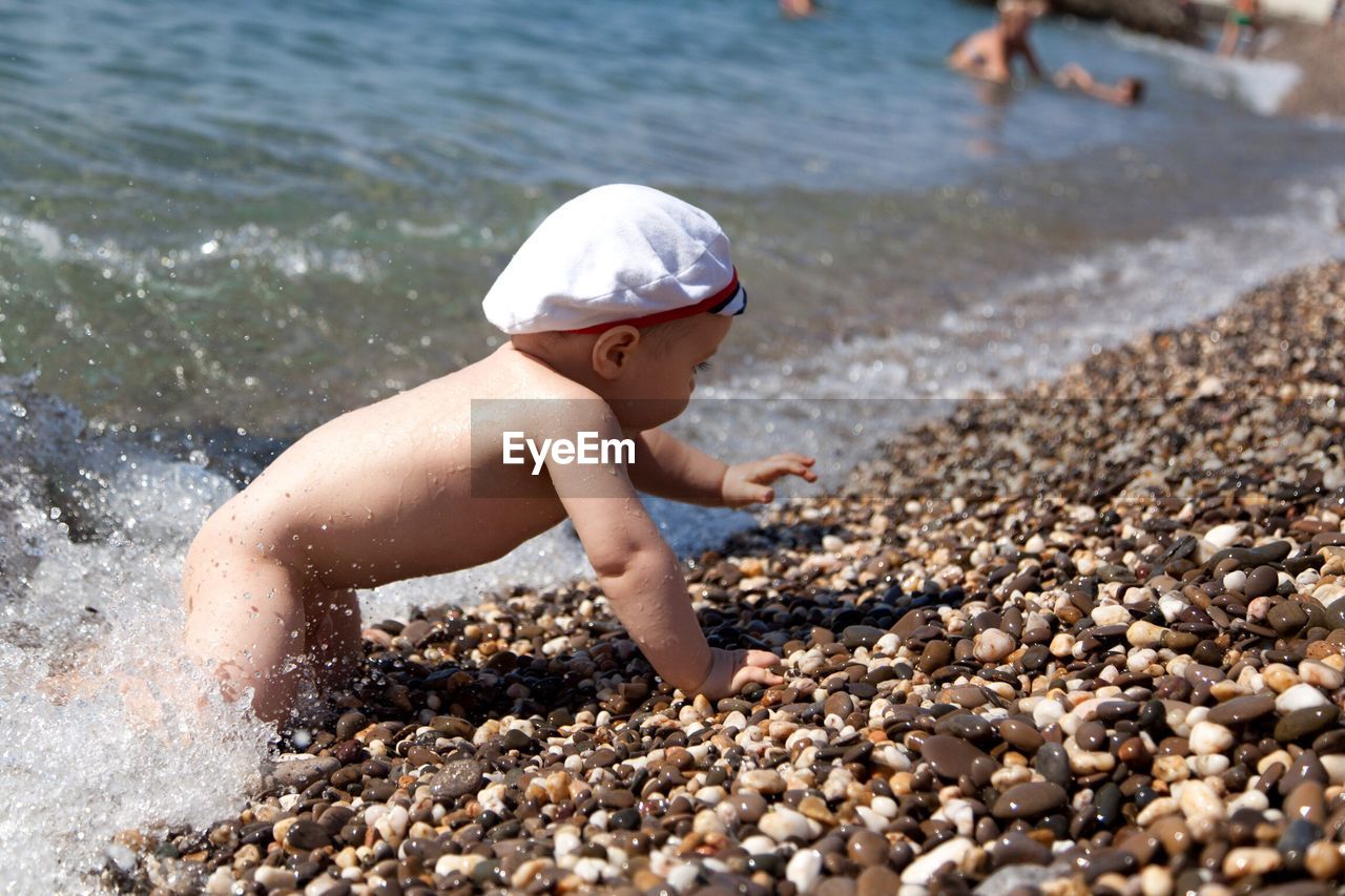 Side view of shirtless baby crawling on shore