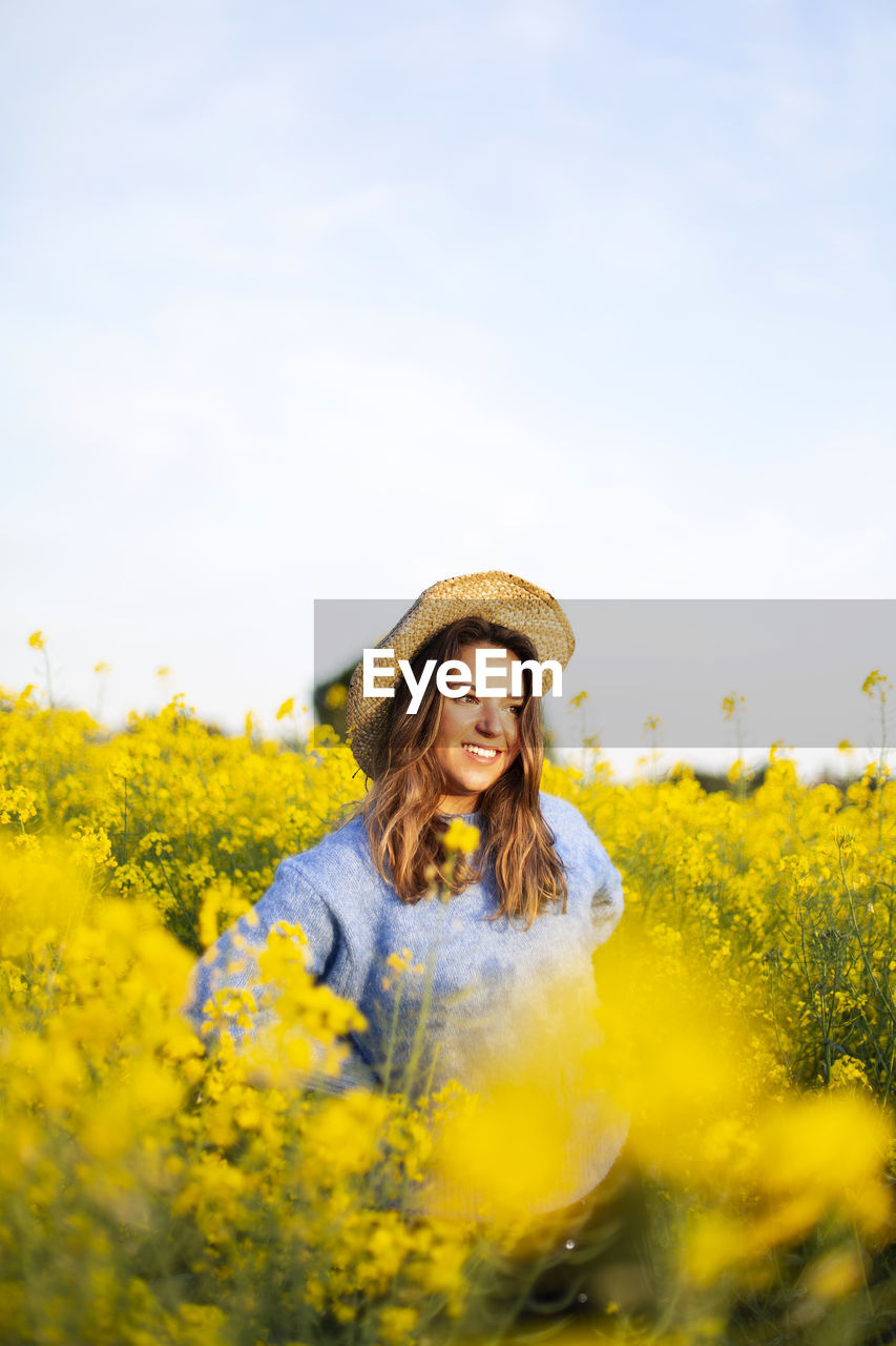 Portrait of smiling young woman with yellow flowers in field against sky