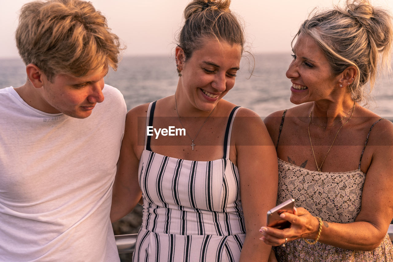 Beautiful mother with her two twenty year old sons take a break by the sea at sunset. summer concept