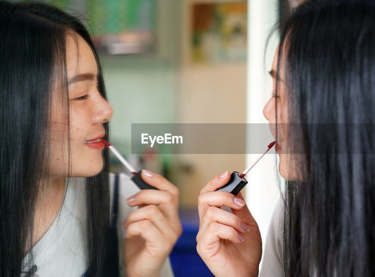 Close-up of woman applying lipstick while looking at mirror