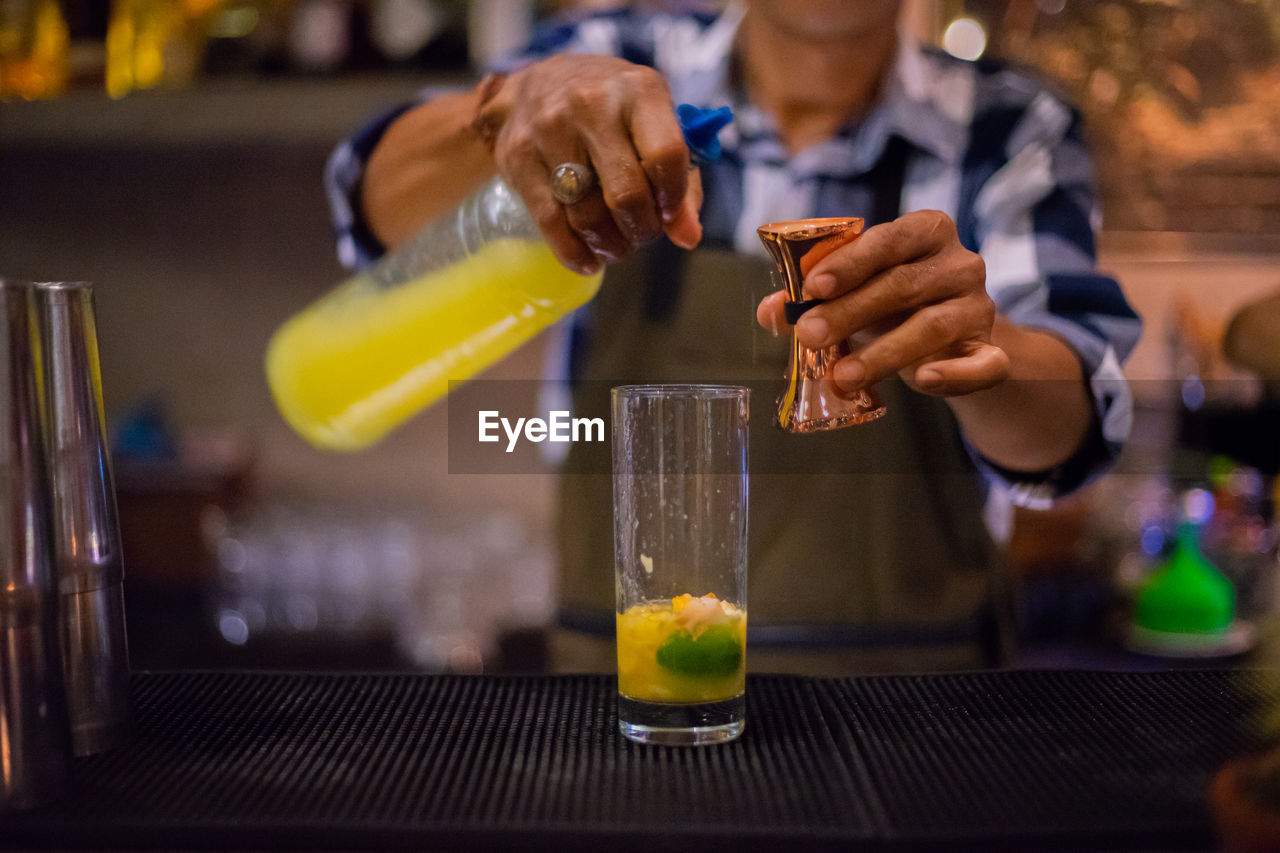 Midsection of bartender preparing drinks while standing in bar