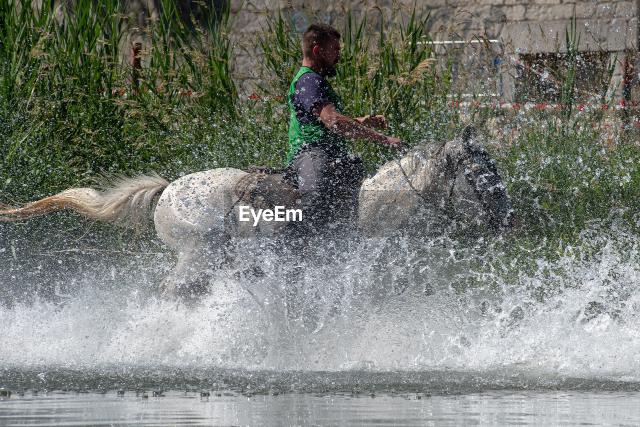 FULL LENGTH OF MAN SPLASHING WATER IN MID-AIR