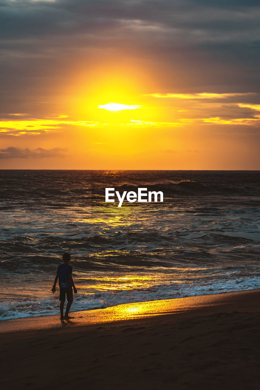 A boy near the shore of a beach at sunset