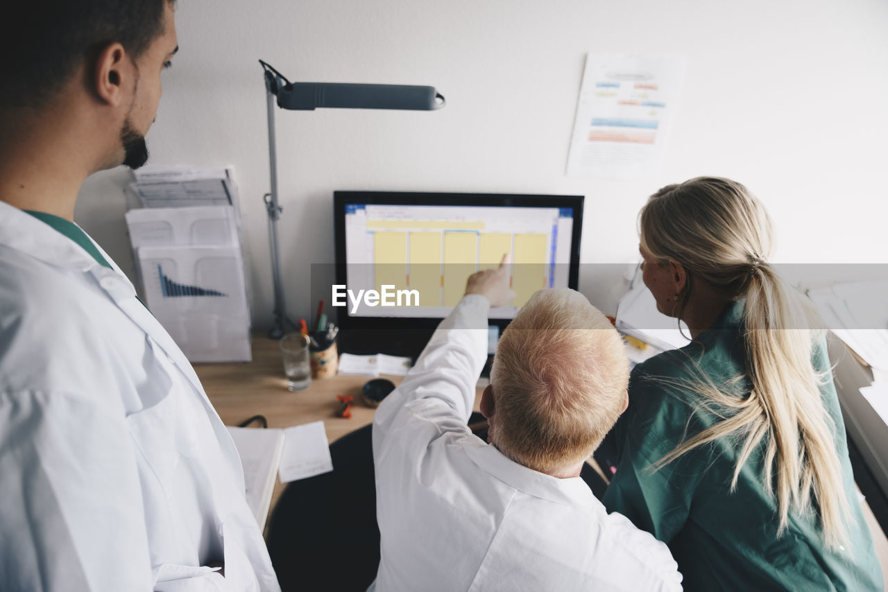 High angle view of female nurse and male doctors discussing over computer at office