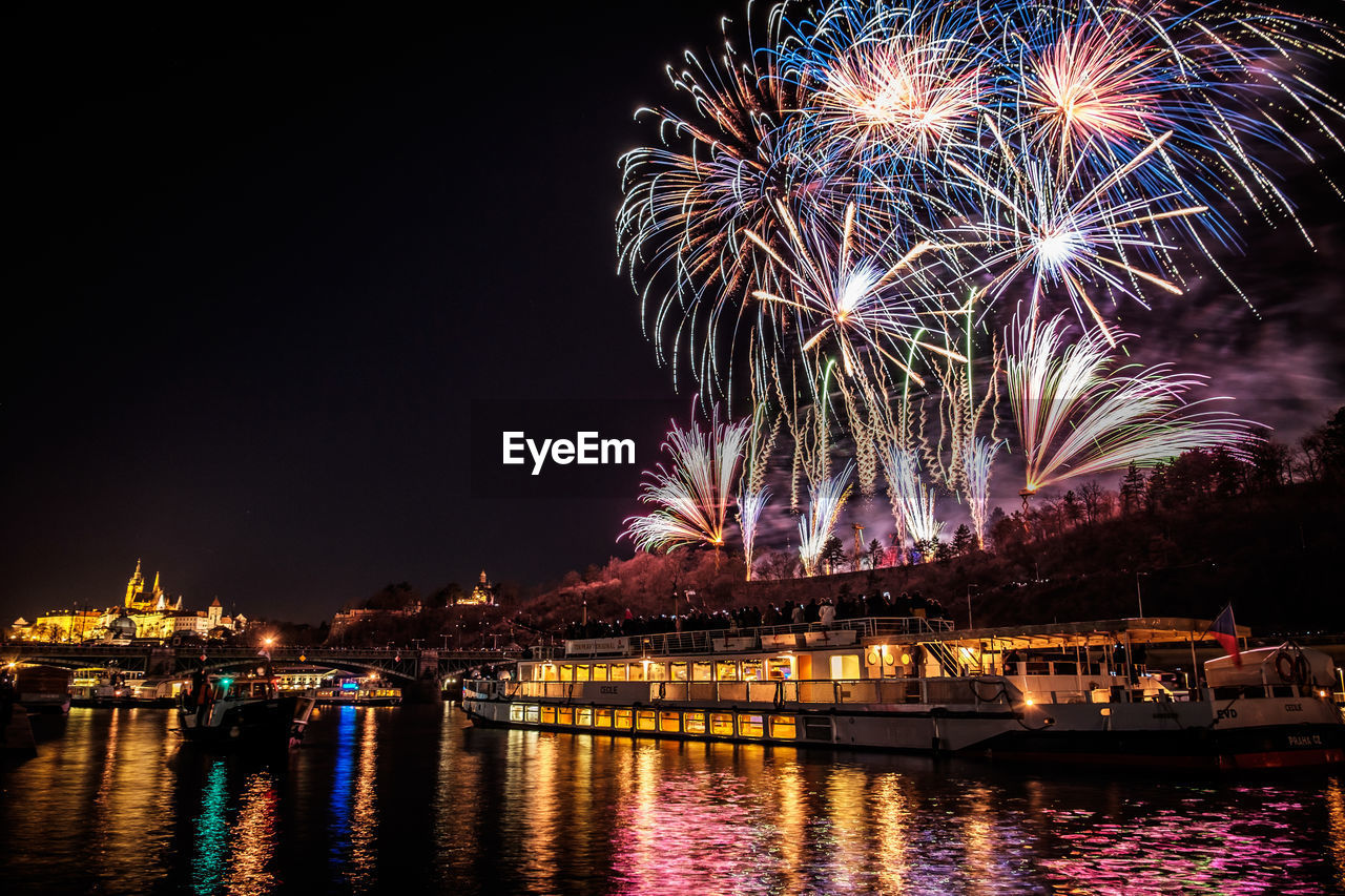 Low angle view of illuminated firework display over river against sky at night