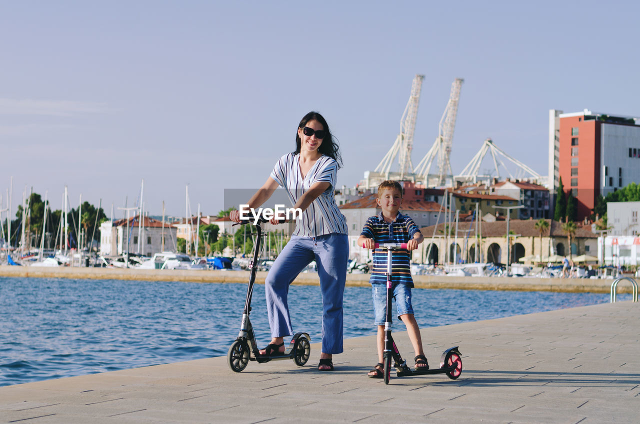 Happy family lifestyle. mother, boy, girl walking in city. ride scooters. laughing on summer. fun