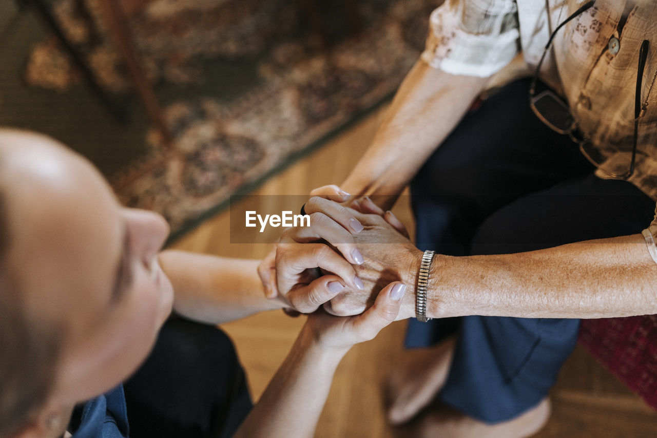 High angle view of senior woman holding hands of female caregiver at home