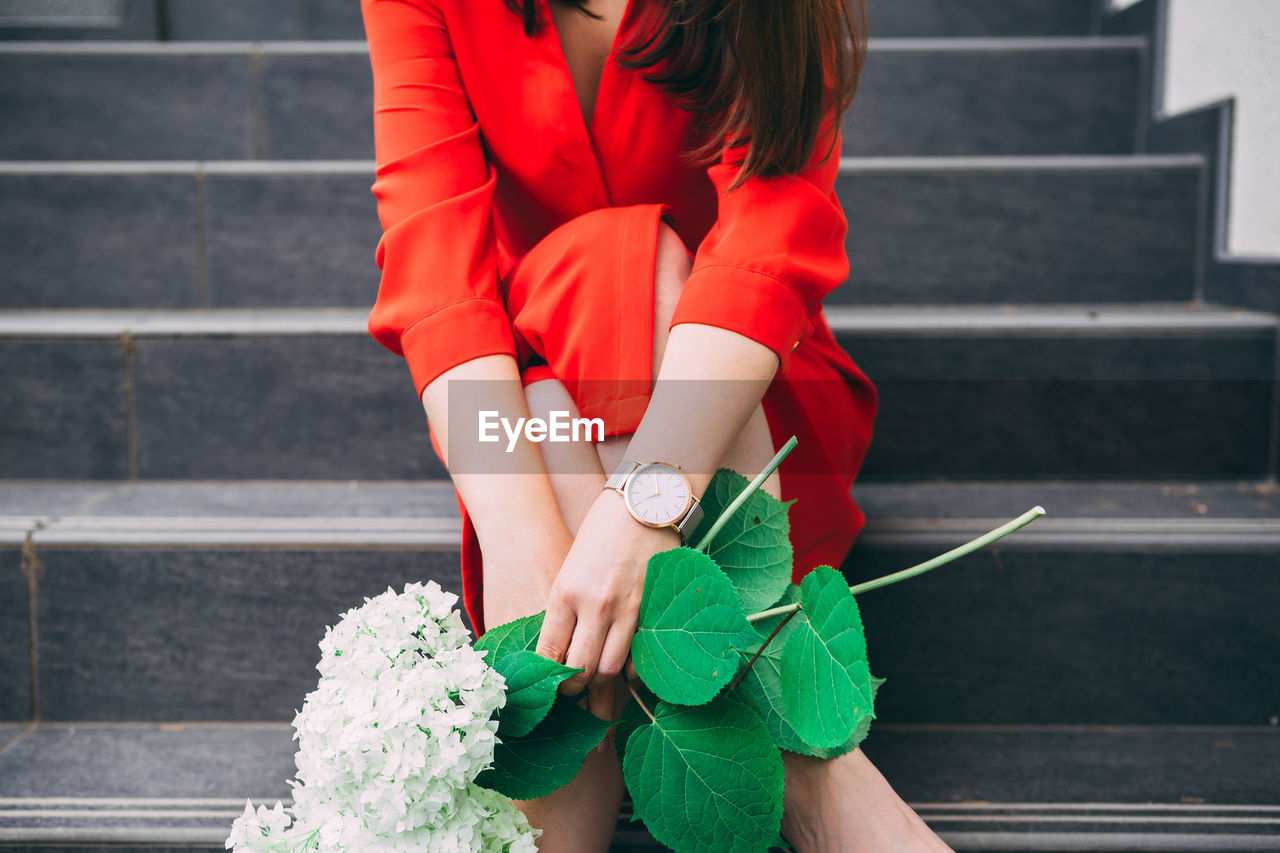 Midsection of woman holding flowers while sitting on steps