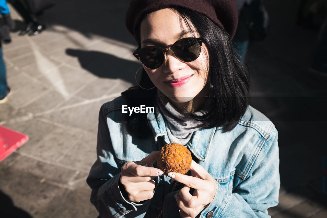 Portrait of smiling woman wearing sunglasses holding sweet food in city