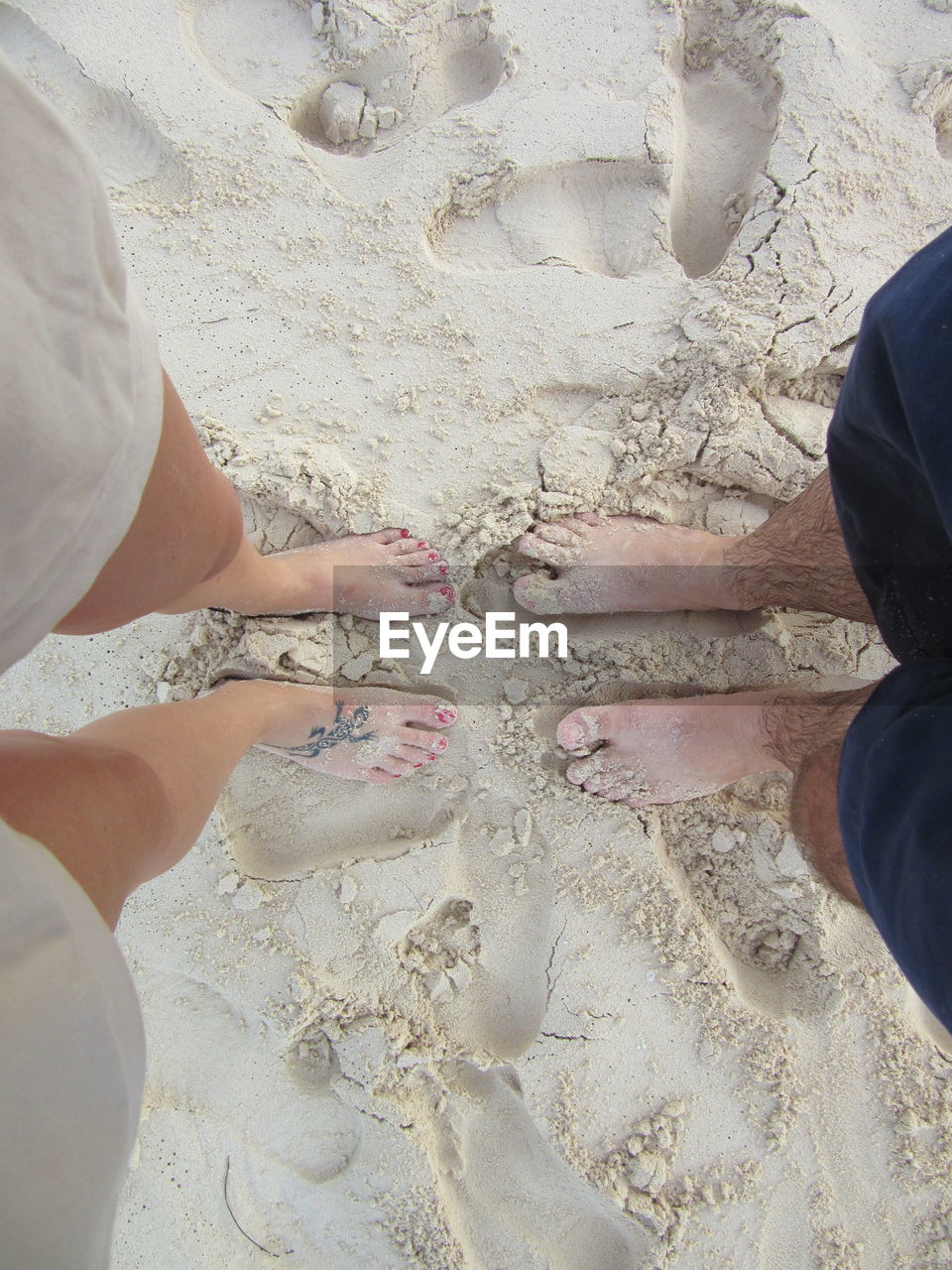 Low section of couple standing on sand at beach