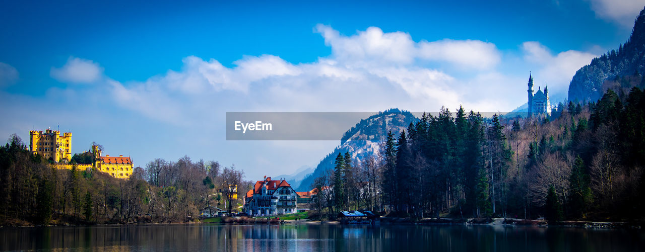 PANORAMIC VIEW OF TREES AND BUILDINGS BY LAKE AGAINST SKY