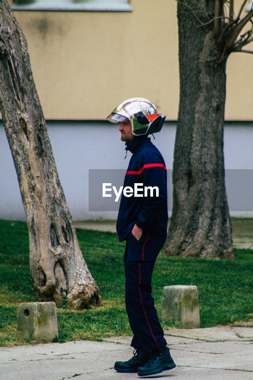 SIDE VIEW OF BOY STANDING BY TREE