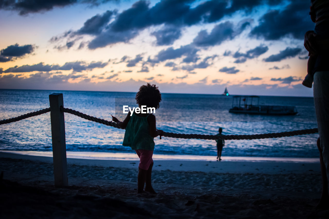 Girl standing at beach against sky during sunset